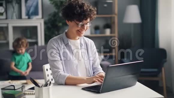 当小男孩在家画手提电脑时微笑着年轻的女自由职业者视频的预览图