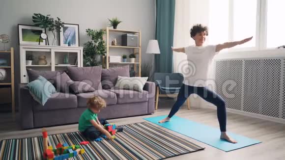 美丽的女孩妈妈做瑜伽时孩子玩玩具地板早上视频的预览图