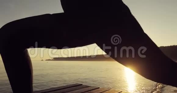 在河边码头上的女人在日落时分的战士I波斯练习瑜伽侧视视频的预览图