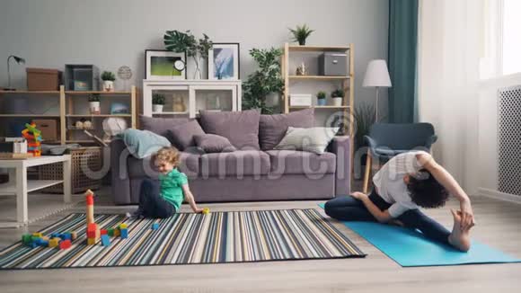 年轻女子在家做瑜伽而小孩在玩木积木视频的预览图