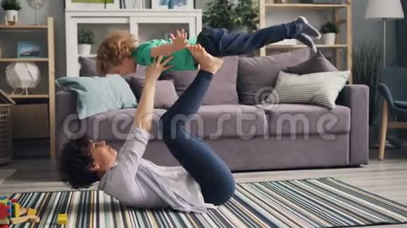 年轻女子用手和腿抱着小男孩笑着玩视频的预览图