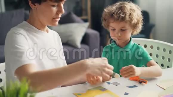 年轻女士教她儿子用纸胶棒和剪刀做拼贴画视频的预览图