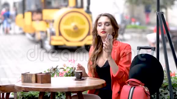 微笑的年轻女子坐在城市的咖啡馆里在打电话视频的预览图