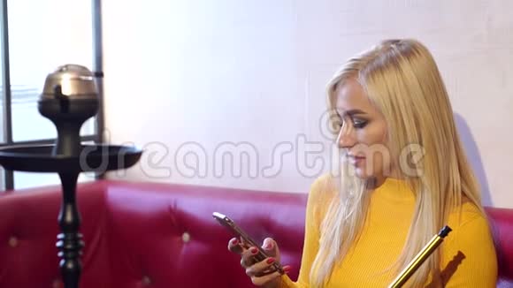 年轻的女孩坐在一个红沙发上的咖啡馆里带着电话和钩子视频的预览图
