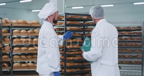 年轻的面包师和主要工程师在一个面包店区进行了一次谈话那里有很多货架上有新鲜的烘焙面包视频的预览图