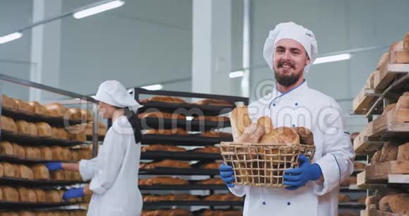 充满魅力的微笑男面包师下巴拿着装满新鲜烘焙面包的篮子直视镜头视频的预览图