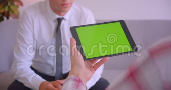 客户服务经理在办公室里用绿色屏幕与客户手持平板电脑交谈的特写照片视频的预览图