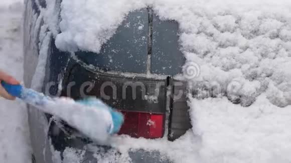 刮擦汽车挡风玻璃上的冰雪女人用刷子擦雪车大雪覆盖了汽车视频的预览图
