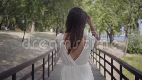 一位身穿太阳镜身穿白色长夏装长裙穿着木制服装的迷人的黑发少女视频的预览图