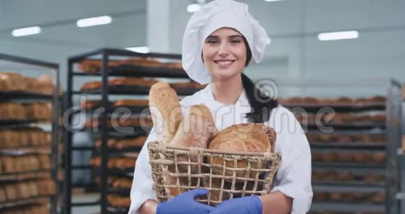 一位乡村女面包师在一家面包店里的肖像镜头前拿着一个篮子和新鲜的烘焙面包视频的预览图