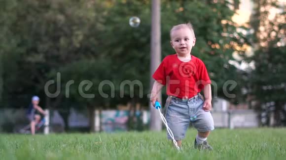 一个可爱的穿着牛仔短裤的婴儿在户外慢动作的肥皂泡后面奔跑视频的预览图