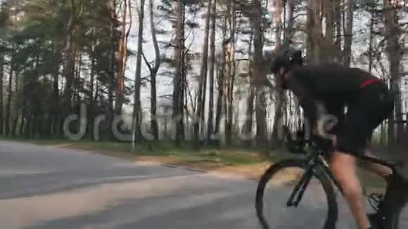 骑自行车的人冲出马鞍作为自行车训练公园穿着黑色的衣服强壮的腿部肌肉慢动作视频的预览图