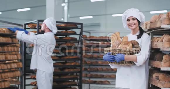 漂亮的面包师女士拿着一大篮子新鲜的有机面包在面包店里直视着镜头的肖像视频的预览图