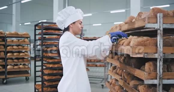 漂亮的女人面包师把面包按顺序放在架子上她穿着漂亮的白色制服面包店视频的预览图