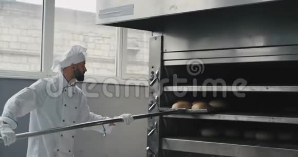专业烘焙厂的面包师厨师穿着特别的厨师制服从烤箱机上取下面包他的帮助视频的预览图