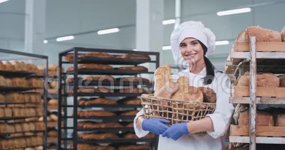 美丽的女士面包师穿着白色制服手里拿着一个篮子里面有新鲜的面包在镜头前笑得很可爱视频的预览图