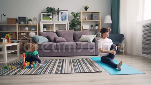 运动女孩在家做瑜伽而她的儿子在玩积木视频的预览图