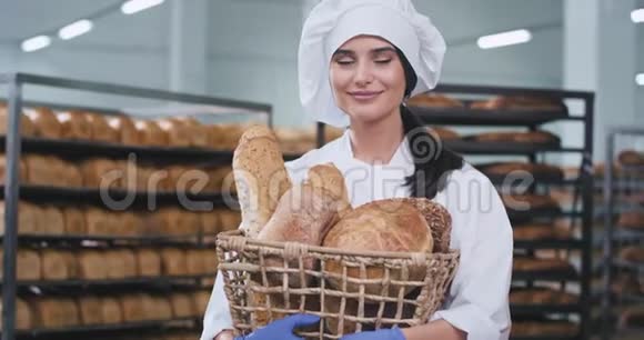 在一个大型的烘焙行业里镜头前的迷人的女士带着美丽的微笑拿着一个带新鲜烘焙的篮子视频的预览图