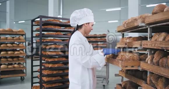 迷人的成熟女人面包师穿着漂亮的白色制服检查新鲜面包并把订单上架视频的预览图