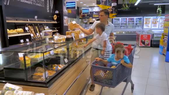 购物背景孩子们坐在购物车里父亲带着两个孩子在超市里转悠视频的预览图