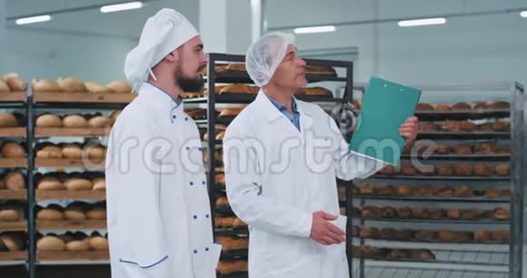 面包业的老工程师和带着下巴的年轻面包师在满是架子的面包店区开会视频的预览图