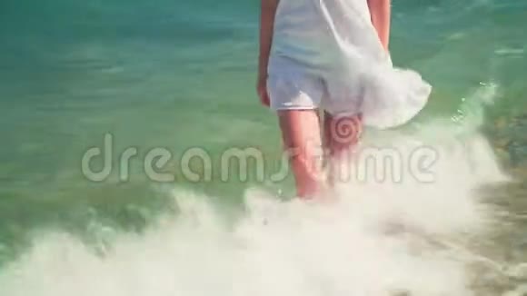 一个穿着白色海滩礼服的女孩站在海边一个光着脚的漂亮女孩站在海边视频的预览图