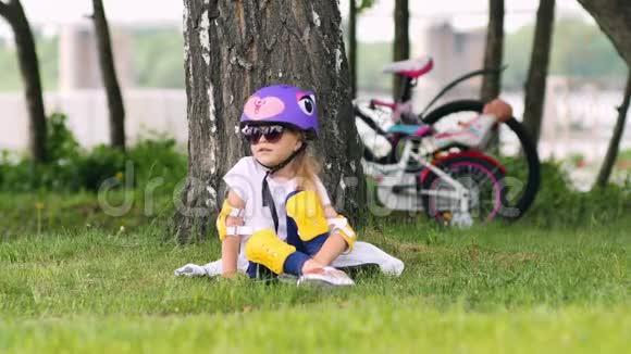 可爱的金发女孩坐在树下戴着自行车头盔视频的预览图