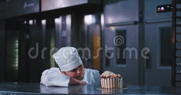 一个有魅力的年轻人带着惊奇的心情挑选着装饰精美的蛋糕而一个大个子男人把一个大托盘推在后面视频的预览图