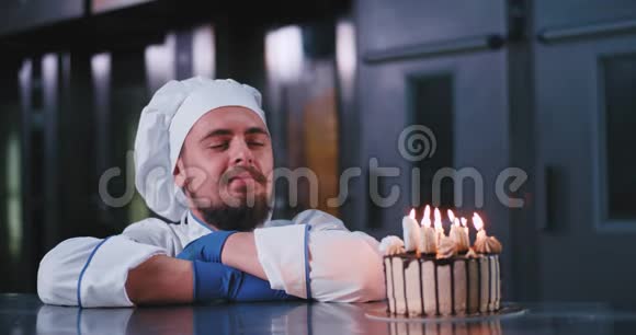 一个戴着厨师帽的迷人男人在神圣的生日蛋糕上吹灭蜡烛视频的预览图