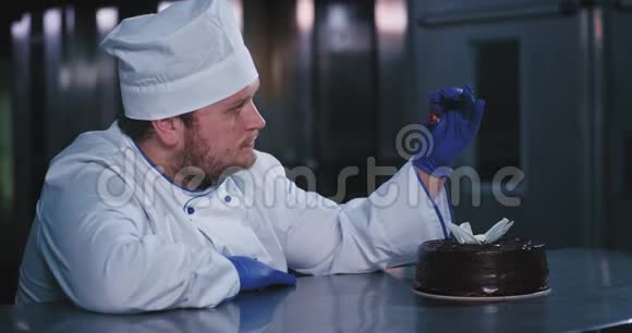 面包大个子男人把樱桃放在蛋糕上双手戴着蓝色手套盯着蛋糕看视频的预览图