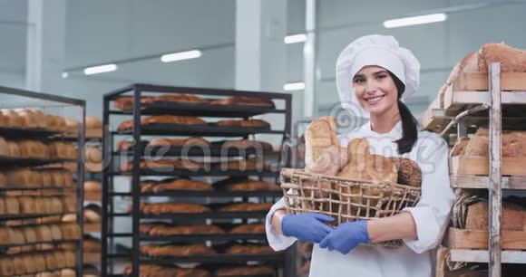 在一家面包厂一位微笑的漂亮女士拿着一大篮新鲜的烤面包在镜头前她看起来很可爱视频的预览图