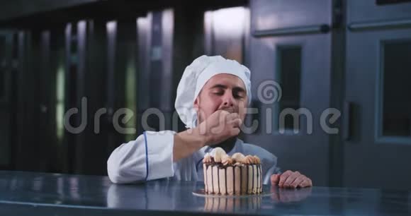 一个长着胡子戴着炊具帽的迷人帅哥用手指在这块美味的蛋糕上挑选视频的预览图