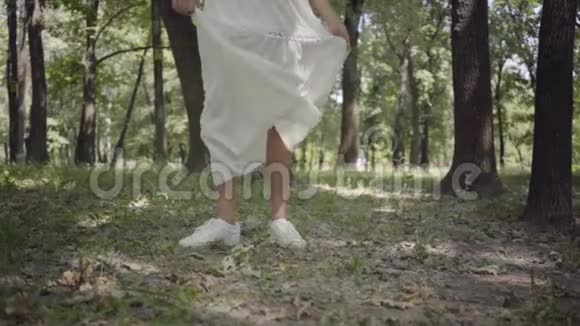 未被认出的年轻女孩穿着白色的长夏礼服在公园里旋转一个漂亮女人在户外休闲视频的预览图