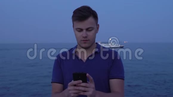 晚上年轻男子在海滨游轮上使用智能手机并以此为背景视频的预览图