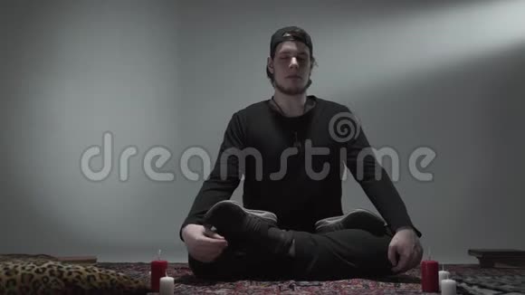 年轻的臀部坐着闭着眼睛盘腿在一个空房间里蜡烛冥想灵性魔力视频的预览图
