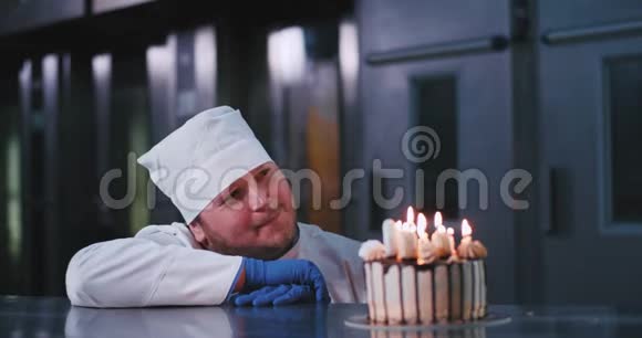 一个长着低胡子的诱人的面包师男子毫不费力地吹灭了装饰精美的生日蛋糕上的蜡烛视频的预览图