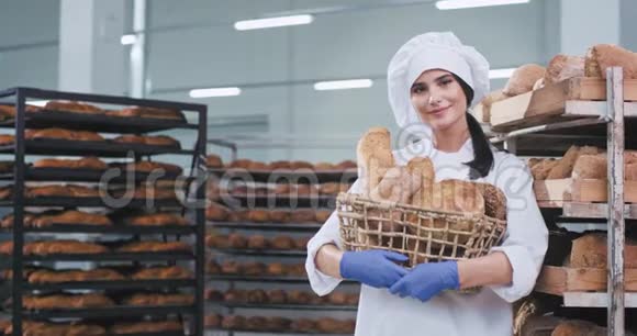 面包行业的年轻女性面包师拿着一篮子新鲜的烘焙面包直视着相机笑得很漂亮视频的预览图