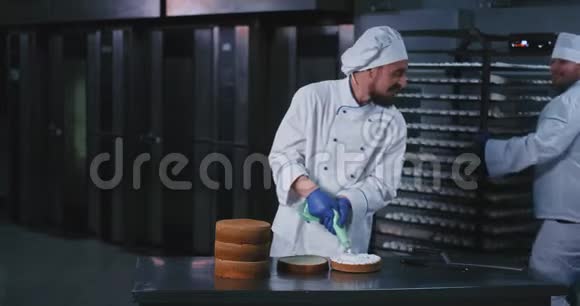 一个胖乎乎的年轻厨师用浅绿色的白色蓬松奶油装饰蛋糕的内部视频的预览图