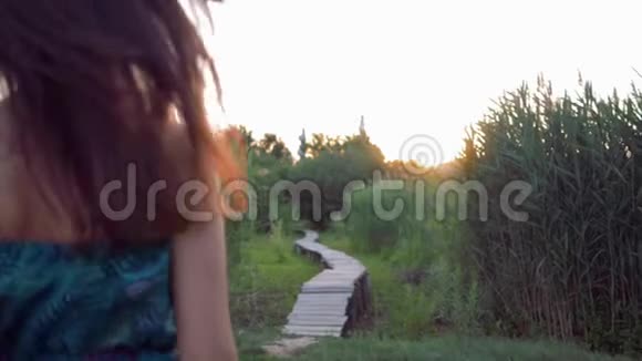 快乐迷人的女孩光着脚在木桥上奔跑在夕阳下的绿草中享受大自然视频的预览图