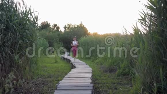 大自然中的跑步运动穿着漂亮的健身服积极运动的女人在户外的木桥上慢跑视频的预览图