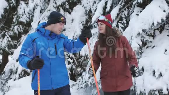 滑雪场上的一对快乐的滑雪者在白雪覆盖的松树附近谈笑风生视频的预览图