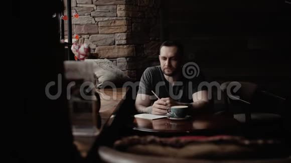 有着胡茬和纹身手臂的野蛮人坐在咖啡馆里做笔记视频的预览图