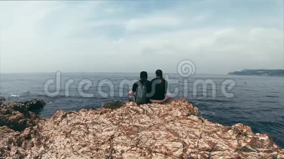 恋爱中的夫妇坐在海边的岩石边缘谈论不同的话题享受风景美丽的时光流逝视频的预览图