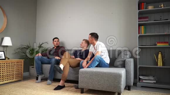 三个快乐的年轻人坐在家里的沙发上愉快地交谈视频的预览图