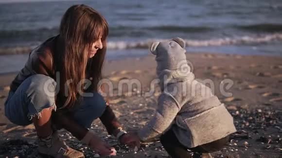可爱的蹒跚学步的孩子和母亲正在一起寻找采摘和收集沙滩上的贝壳视频的预览图