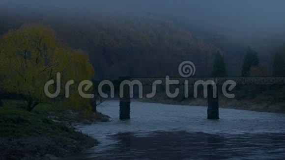 雾蒙蒙的夜晚越过河流的老桥视频的预览图