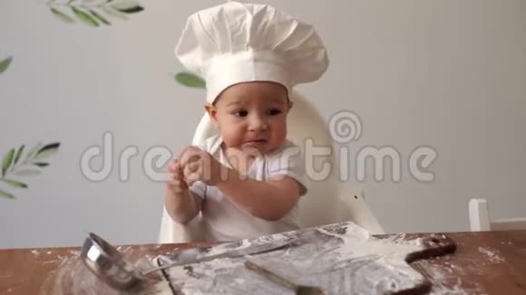 一个戴着厨师帽小可爱男孩坐在有面粉的桌子旁吃饼干视频的预览图
