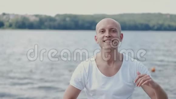 穿着白色T恤在湖边跳舞的秃头肖像视频的预览图