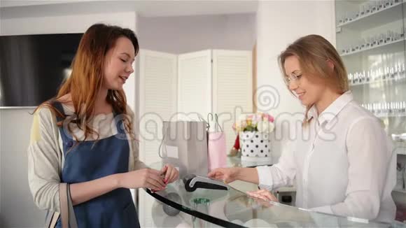 在时尚陈列室用信用卡付款的快乐女人顾客年轻女孩付钱买她的东西视频的预览图