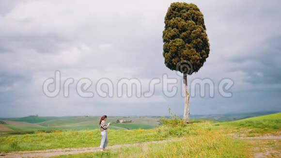 一个年轻的女人站在一棵大树附近拍照视频的预览图
